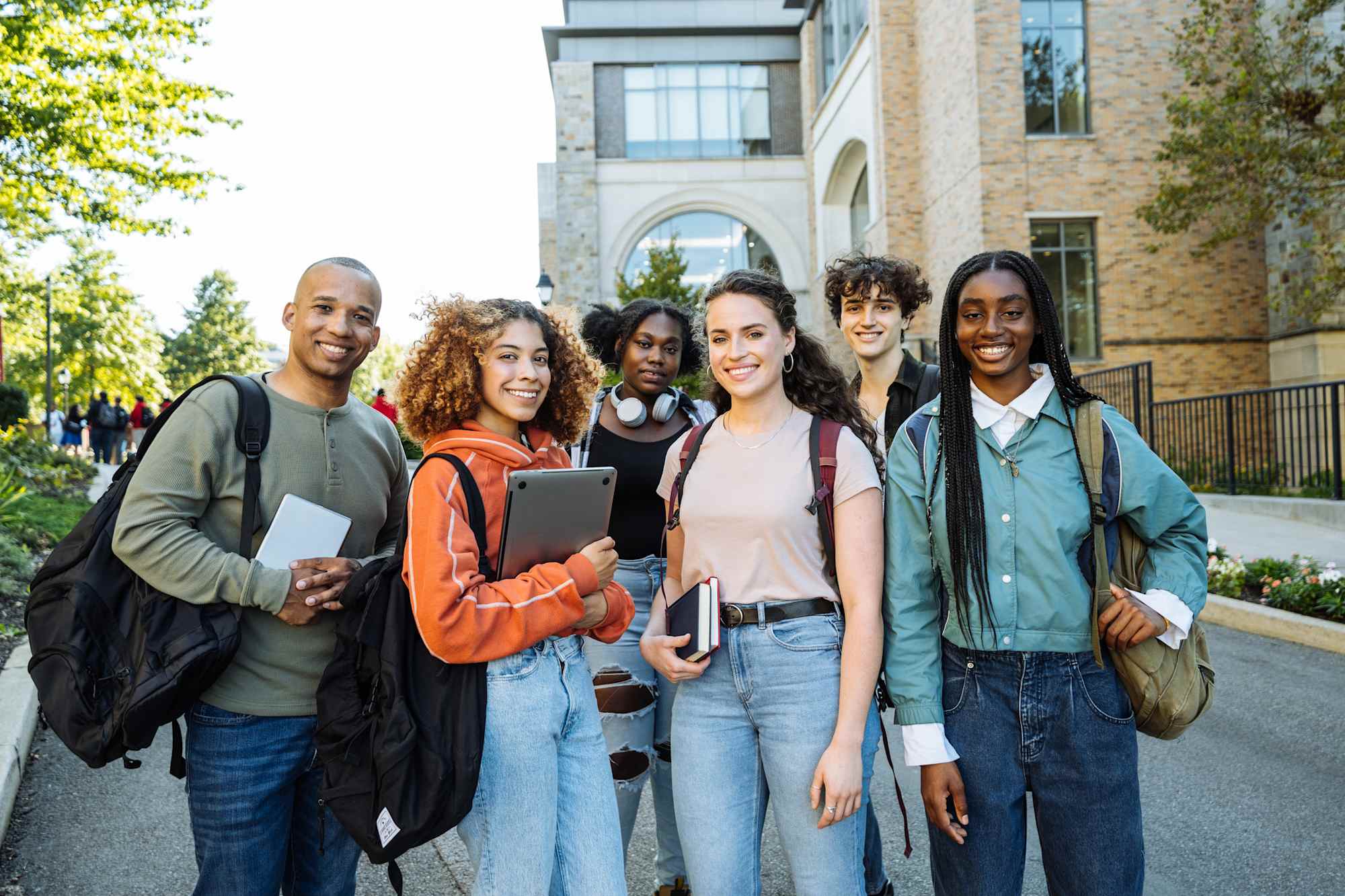 A diverse group of students and an educator smiling together on a campus walkway