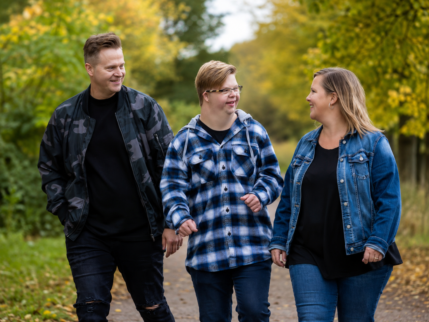 A father, son, and mother walking together along a tree-lined path, smiling