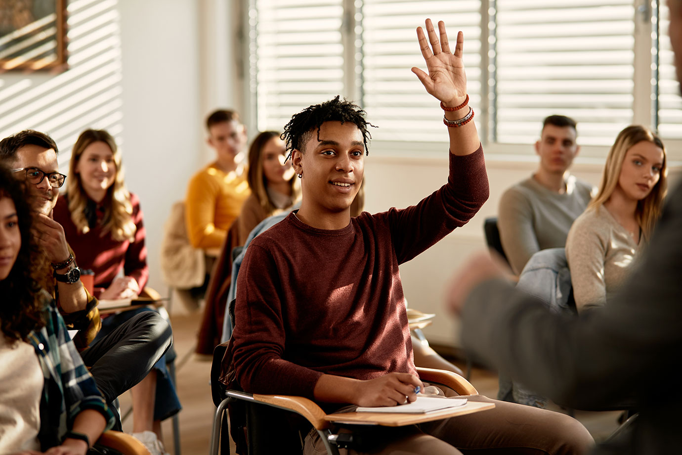 A student raising a hand in a bright classroom discussion